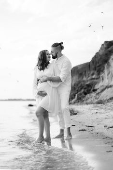 a guy with a girl in white clothes on the seashore next to clay cliffs