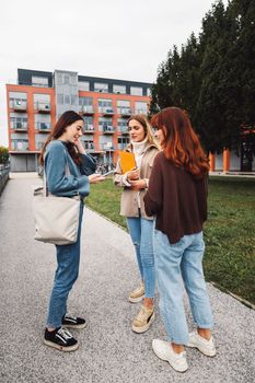 Group of three cheerful female collage students outside their dorm on a cold autumn day, walking on campus to get to their class. 