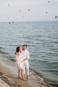 a guy with a girl in white clothes on the seashore next to clay cliffs