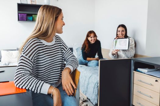 Group of three roommates, college student, young caucasian women, spending time together in their room, studying, talking, having fun, laughing. 