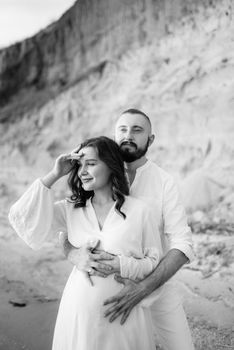 a guy with a girl in white clothes on the seashore next to clay cliffs