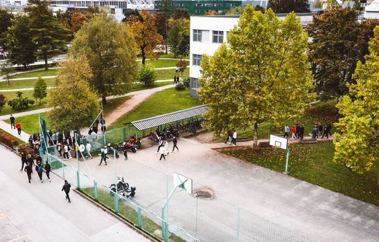 Aerial view of students walking outdoors on campus going to and out of class. Autumn day, lots of trees and green grass on campus. 