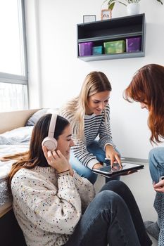 Group of three roommates, college student, young caucasian women, spending time together in their room, studying, talking, having fun, laughing. 