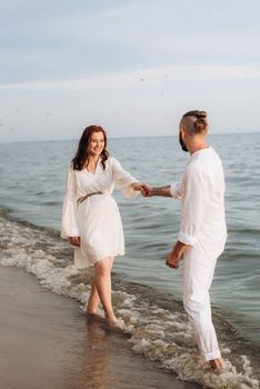 a guy with a girl in white clothes on the seashore next to clay cliffs