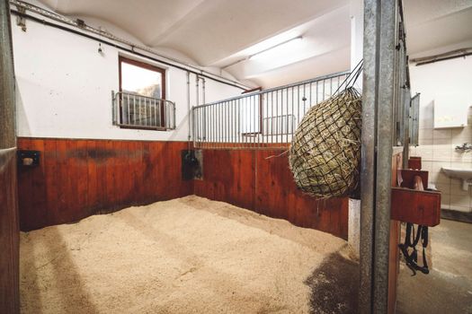 Empty stable, no horses inside the stables. Clean and empty horse boxes with fresh hay at the ranch. 