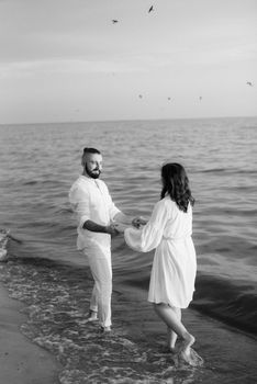 a guy with a girl in white clothes on the seashore next to clay cliffs