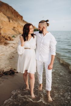 a guy with a girl in white clothes on the seashore next to clay cliffs