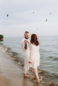 a guy with a girl in white clothes on the seashore next to clay cliffs