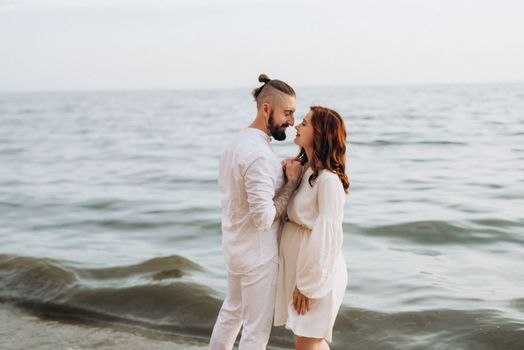 a guy with a girl in white clothes on the seashore next to clay cliffs