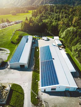 Solar panels installed on a roof of a large industrial building or a warehouse. Industrial building in the country side of Slovenia with residential houses in the background. High quality photo