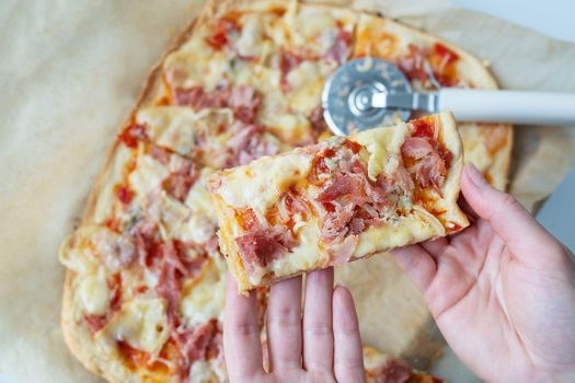 Juicy delicious slice of pizza with ham, onion and cheese. Pizza knife on the background. Cooking pizza at home, the girl holds a piece of pizza in her hands