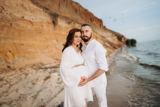 a guy with a girl in white clothes on the seashore next to clay cliffs