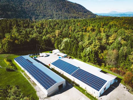 Solar panels installed on a roof of a large industrial building or a warehouse. Industrial building in the country side of Slovenia with residential houses in the background. High quality photo