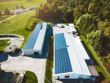 Solar panels installed on a roof of a large industrial building or a warehouse. Industrial building in the country side of Slovenia with residential houses in the background. High quality photo