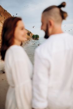 a guy with a girl in white clothes on the seashore next to clay cliffs