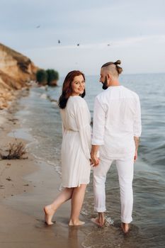 a guy with a girl in white clothes on the seashore next to clay cliffs