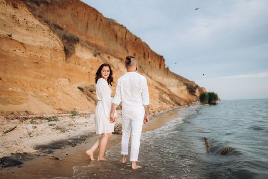 a guy with a girl in white clothes on the seashore next to clay cliffs