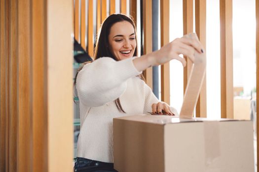 Cheerful young woman excited over a package she just received. Woman getting her christmas gift in the mail. Opening the Christmas present at home.