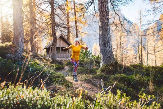 Joyful woman hiker running in the autumn forest, wearing an orange shirt and colorful leggings. Woman jumping in the air while hiking trough the forest. Sunny autumn hike.