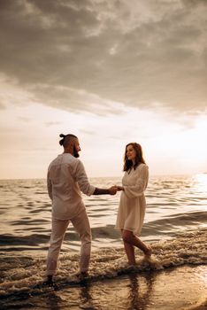 a guy with a girl in white clothes on the seashore next to clay cliffs