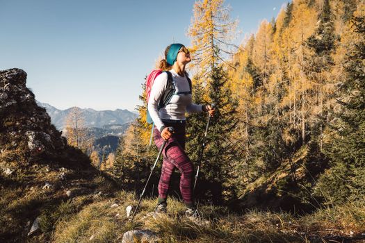 Caucasian woman hiker with hiking poles, hiking on a sunny autumn day somewhere in European Alps. 