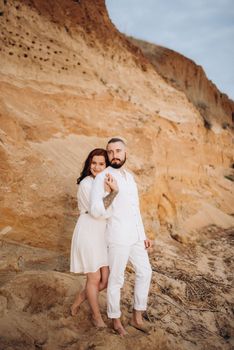 a guy with a girl in white clothes on the seashore next to clay cliffs