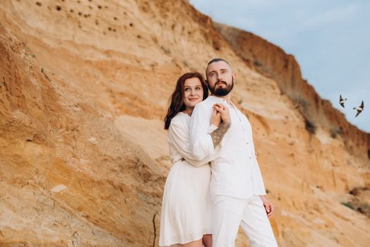 a guy with a girl in white clothes on the seashore next to clay cliffs