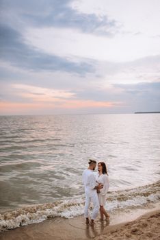 a guy with a girl in white clothes on the seashore next to clay cliffs