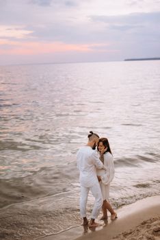 a guy with a girl in white clothes on the seashore next to clay cliffs