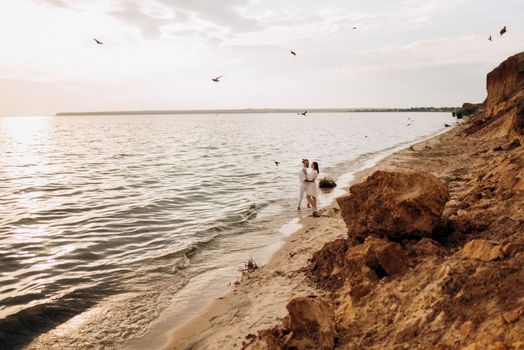 a guy with a girl in white clothes on the seashore next to clay cliffs