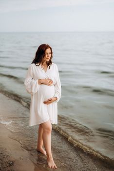 pregnant girl with brown hair on the seashore in white clothes