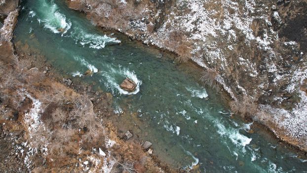 The Grand Canyon in the steppe with the emerald river. A crack in the ground with black stones, the green color of the river. Bushes grow in places. There are tourists and buses on edge. Kazakhstan