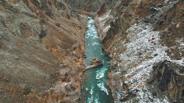 The Grand Canyon in the steppe with the emerald river. A crack in the ground with black stones, the green color of the river. Bushes grow in places. There are tourists and buses on edge. Kazakhstan