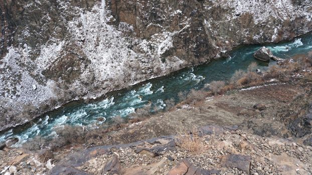 The Grand Canyon in the steppe with the emerald river. A crack in the ground with black stones, the green color of the river. Bushes grow in places. There are tourists and buses on edge. Kazakhstan