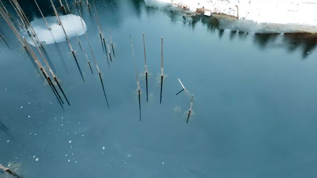 Kaindy Mountain Lake in winter. Drone view of the freezing dark water. Trunks of frozen fir trees come out of the lake. There is a coniferous forest and mountains covered with white snow all around