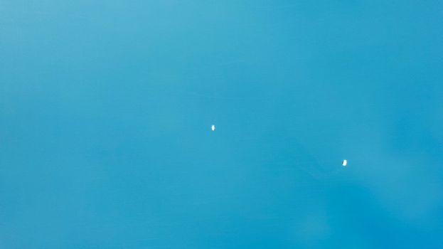 Top view of the turquoise surface of the lake water. A small ripple from the waves and a slight gradient from light blue to dark blue. Photo as a background. There is a boat and a catamaran floating