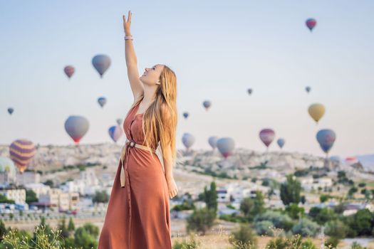 Tourist woman looking at hot air balloons in Cappadocia, Turkey. Happy Travel in Turkey concept. Woman on a mountain top enjoying wonderful view.