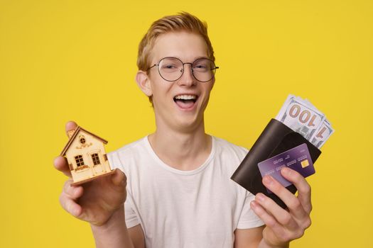Financing Home Purchase Concept. A happy young man holds in his hands a wallet with money and a credit card to buy his home. High quality photo