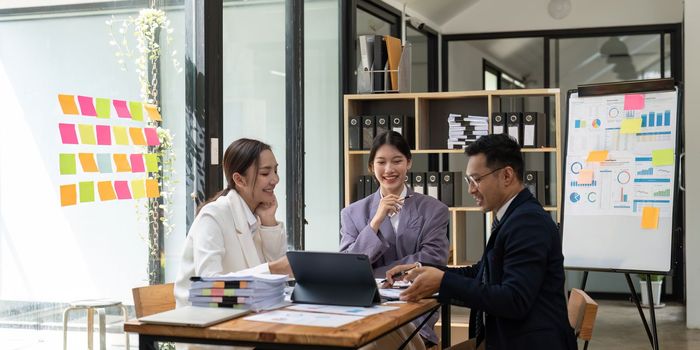 Group of young Asian business people brainstorming, looking at laptop computer.