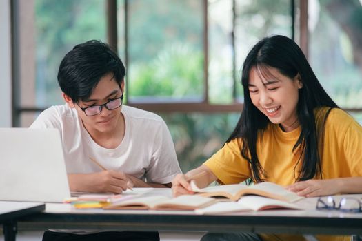 Young asian university students are studying for an exam. There are tutor books with friends. They are classmates that try to help each other. They have been tutoring for many hours in the campus.