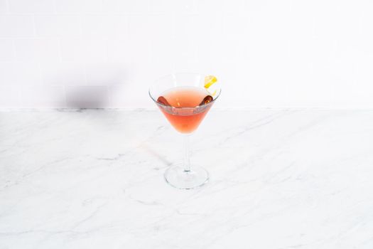 Cosmopolitan cocktail in a martini glass and decorated with a lemon swirl.
