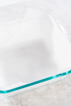 Lining square cheesecake pan with parchment paper sheet to prepare candy corn fudge.