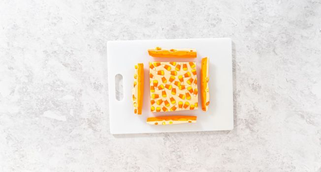 Flat lay. Cutting candy corn fudge into square pieces on a white cutting board.