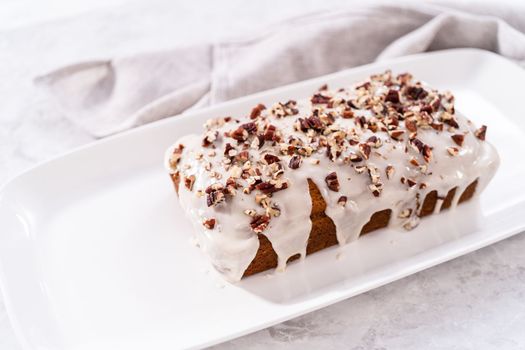Sliced homemade pumpkin bread with a white glaze and pecans on a white serving tray.