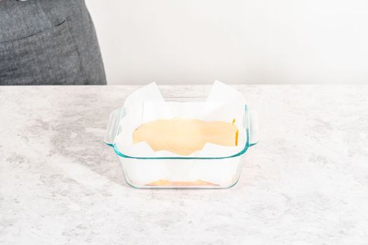 Pouring fudge mixture into the square glass baking pan lined with parchment paper to prepare candy corn fudge.