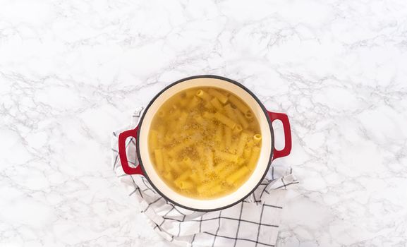Flat lay. Boiling pasta in an enameled dutch oven to prepare chicken alfredo pasta.