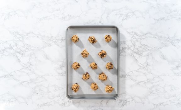 Flat lay. Scooping cookie dough with dough scoop into a baking sheet lined with parchment paper to bake soft oatmeal raisin walnut cookies.