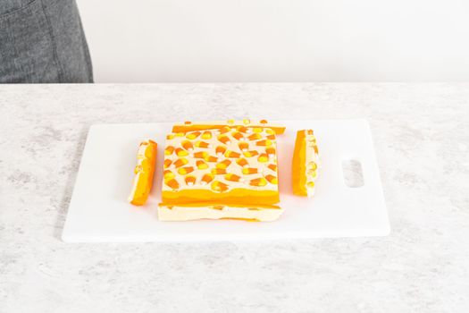 Cutting candy corn fudge into square pieces on a white cutting board.