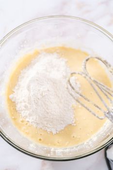 Mixing ingredients in a large glass mixing bowl to bake apple bundt cake with caramel glaze.