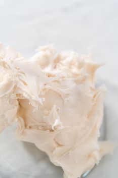Whisking store-bought buttercream frosting with an electric hand mixer to decorate gingerbread bundt cake with caramel filling.